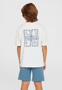 T-shirt en coton blanc avec un imprimé graphique bleu et des accents à motifs au dos, associé à un short bleu. Manches courtes et coupe décontractée.