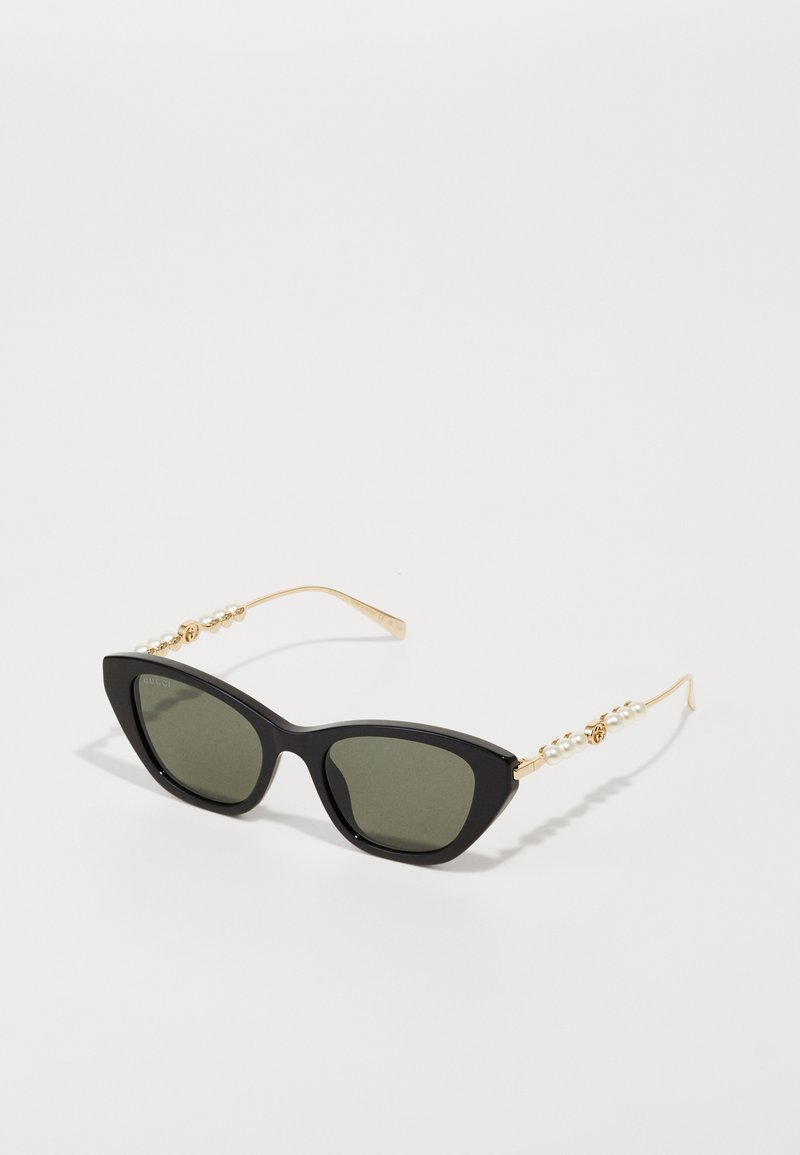 Kattöga solglasögon med svarta bågar, grå linser och guldmetallarmar med en pärlliknande detalj. Slät yta och vinkelaktig design.