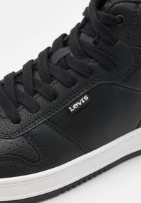 Sneaker in pelle nera con finitura texturizzata, lacci neri, suola bianca e un piccolo logo Levis sul lato.