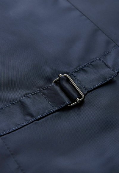 Marinblått textil med en slät yta har en metallspänne och en sydd rem, vilket skapar en funktionell stängningsdetalj.