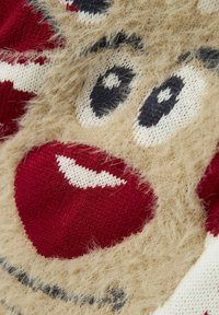 Gros plan sur un visage de renne en tricot flou avec de grands yeux noirs et blancs, un nez rouge et une bouche souriante sur un pull de Noël.