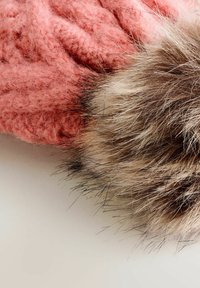 Różowa dzianina o teksturowanym wzorze obok miękkiego, puszystego, wielokolorowego pom-pom z futra na jasnej powierzchni.