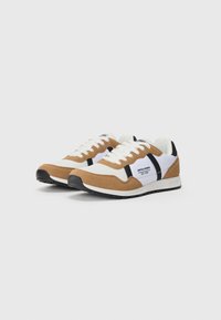 Par med brune og hvite casual sneakers med svarte aksenter, hvite snørebånd og merkeprofilen "JACK & JONES EST. 1990" på sidepanelene.