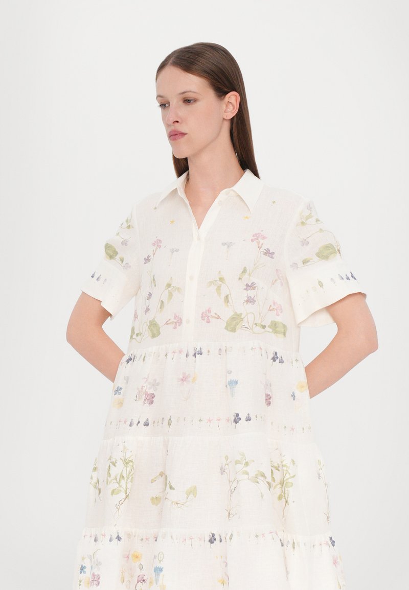 Robe en lin à manches courtes, col boutonné, base blanche, avec des impressions florales multicolores sur l'ensemble, présentant un design à ourlet en étages.