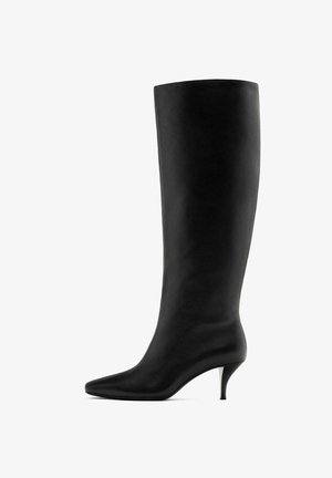 Černá kožená bota po kolena s špičatou špičkou a jehlovým podpatkem. Hladká textura s elegantním, vertikálním designem. Žádné viditelné kovové prvky.