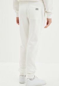 Witte katoenen sweatpants met ribboorden, een achterzak met een logo-opdruk en een relaxed fit. Gecombineerd met witte sneakers.