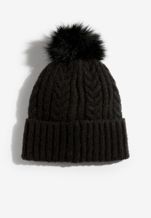 Melna adīta cepure ar ribotu rakstu, uz augšu rotāta ar pūkainu melnu bumbu. Materiāls šķiet mīksts un biezs, lai saglabātu siltumu.