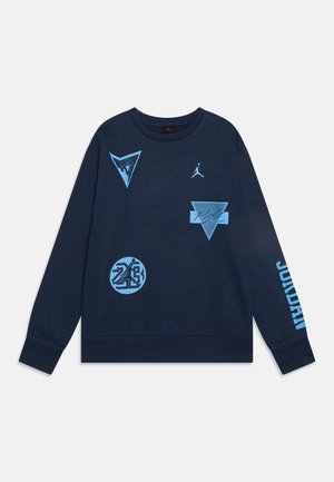 Sweatshirt bleu marine en coton, présentant plusieurs logos et motifs bleu clair, dont un grand texte "JORDAN" sur la manche.