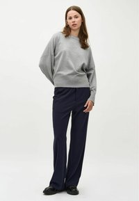 Felpa grigia chiara con spalle drop, orlo a coste, abbinata a pantaloni a gamba larga blu scuro, indossata con scarpe nere. Design minimalista.