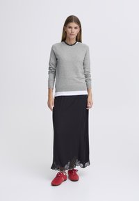 Siv dolg rokav pulover, oblečen čez belo srajco, kombiniran s črno maksi krilo z čipkastim robom in rdečimi športnimi čevlji.