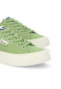 Sneakers in tela verde con suole in gomma bianca, dotati di punta rotonda, occhielli in metallo e dettagli a scacchi sulla linguetta.