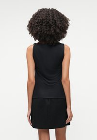 Μαύρη αμάνικη τοπ με απαλό, ελαστικό ύφασμα, που διαθέτει μια διακριτική ρυτίδωση στο πίσω μέρος και ενισχύεται από μεταλλικά στοιχεία στους ώμους.