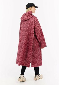 Lyserød vandtæt oversized frakke med hætte, der har et sorte uregelmæssige prikmønster, lange ærmer og sideskafter for bedre bevægelsesfrihed.