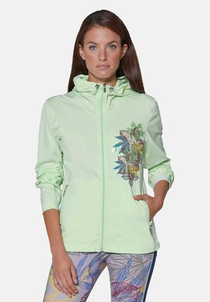 Helle grüne Zip-Jacke mit Kapuze, featuring ein florales Design auf der linken Seite und seitlichen Taschen, aus einem glatten, dehnbaren Stoff.