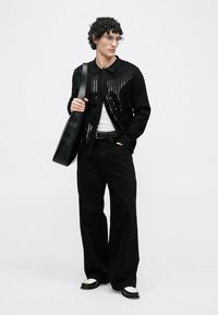 Cárdigan negro con detalles de lentejuelas, usado sobre una camisa blanca, combinado con pantalones negros holgados y zapatos negros con acentos blancos.