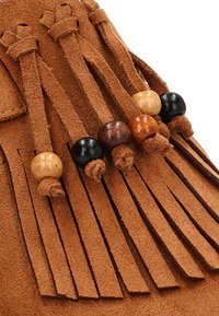 Mocasines de ante marrón con flecos y cuentas de madera decorativas en diferentes tonalidades. Superficie texturizada y detalles de diseño en capas visibles.