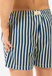 Männerschwimmshorts in einem vertikalen Streifenmuster aus Marineblau und Creme. Mit einem elastischen Bund und einem Label auf der Rückseite. Aus leichtem Material.