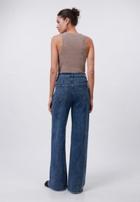Débardeur côtelé marron clair associé à un jean en denim bleu à jambes larges avec une taille haute, des poches arrière et un ourlet effiloché.