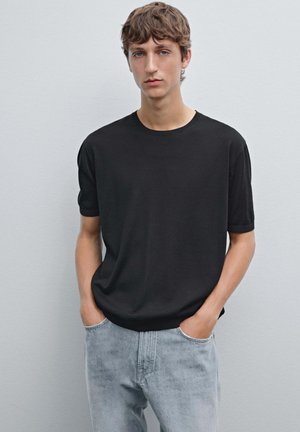 Black short-sleeve t-shirt with a round neckline, made of soft fabric, paired with light blue faded jeans. Simple, clean-cut design.