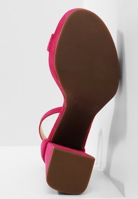 Fuchsia suède sandaal met hoge hak, open teen, enkelriem en een bruine, getextureerde rubberen zool.