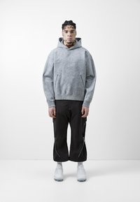 Grå hettegenser med sidelommer, parret med svarte avkortede bukser med sidelommer. Hvit joggesko fullfører antrekket.