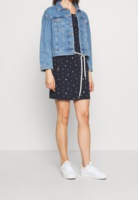 Dżinsowa kurtka, krótki krój, jasnoniebieska, z guzikami z przodu i dwiema kieszeniami na piersi. Granatowa sukienka z regulowanym w pasie ściągaczem i wzorzystymi akcentami. Białe trampki.