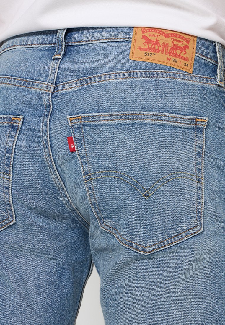 Jean en denim bleu clair avec une coupe droite. Les caractéristiques incluent une patch en cuir sur la ceinture, deux poches arrière et un onglet rouge.