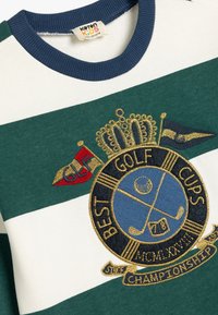Gröna och vita randiga sweatshirt med marinblå ribbad krage, med en guld- och marinblå broderad golfinsignia. Mjuk bomullsmaterial.