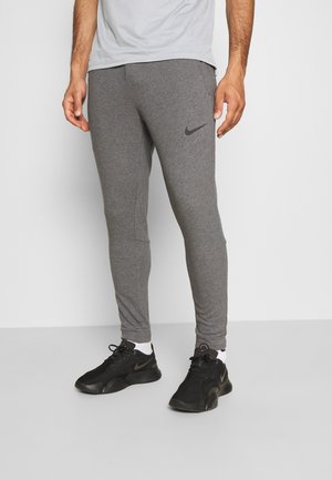 Grijze sportbroek met een slim fit, gemaakt van zacht materiaal. Bevat een zwart Nike-logo op het bovenbeen en ribbelige enkelboorden. Zwarte sneakers gedragen.