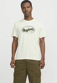 Lichtbeige katoenen t-shirt met korte mouwen en een ronde halslijn, voorzien van een zwart "Originals" logo in een ovale omtrek aan de voorkant.