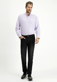 Jasnofioletowa koszula z guzikami, zestawiona z czarnymi dżinsami i szarymi butami sportowymi. Koszula ma subtelny wzór i długie rękawy.