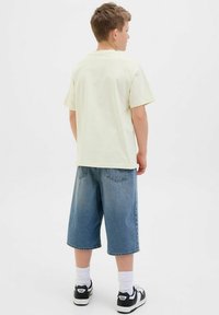 Light yellow short-sleeve t-shirt paired with blue denim shorts, featuring a loose fit and a straight cut, worn with white socks and black shoes.