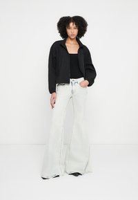 Μαύρο ελαφρύ μπουφάν bomber με φερμουάρ μπροστά, συνδυασμένο με ψηλόμεσα, φαρδιά τζιν παντελόνια σε ανοιχτό μπλε χρώμα. Λείες υφές και μινιμαλιστικός σχεδιασμός.