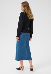 Black textured long-sleeve top paired with a blue denim maxi skirt featuring a straight cut and visible stitching details. Black heeled mules.