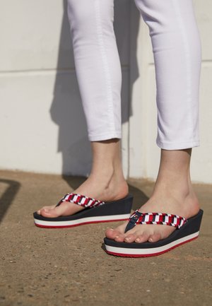 Klapki na koturnie z granatowo-białym paskiem w paski, z czerwonym akcentem. Podeszwa jest gruba, z białą i czerwoną warstwą, co zapewnia wysokość.