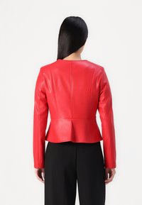Rotem Leder-Peplum-Jacke mit langen Ärmeln und rundem Ausschnitt, die vertikale Nähte und eine glatte Textur aufweist. Schwarze Hosen sind darunter sichtbar.