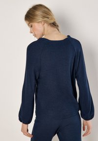 Marineblauer strukturierter Pullover mit langen, luftigen Ärmeln und einem runden Ausschnitt, der eine lockere Passform und ein dezentes Strickmuster aufweist.