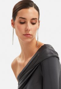 Asymmetrische grijze zijden top met gedrapeerde textuur, met een een-schouder ontwerp. Lange zilveren oorbellen voegen een stijlvolle, moderne accent toe.