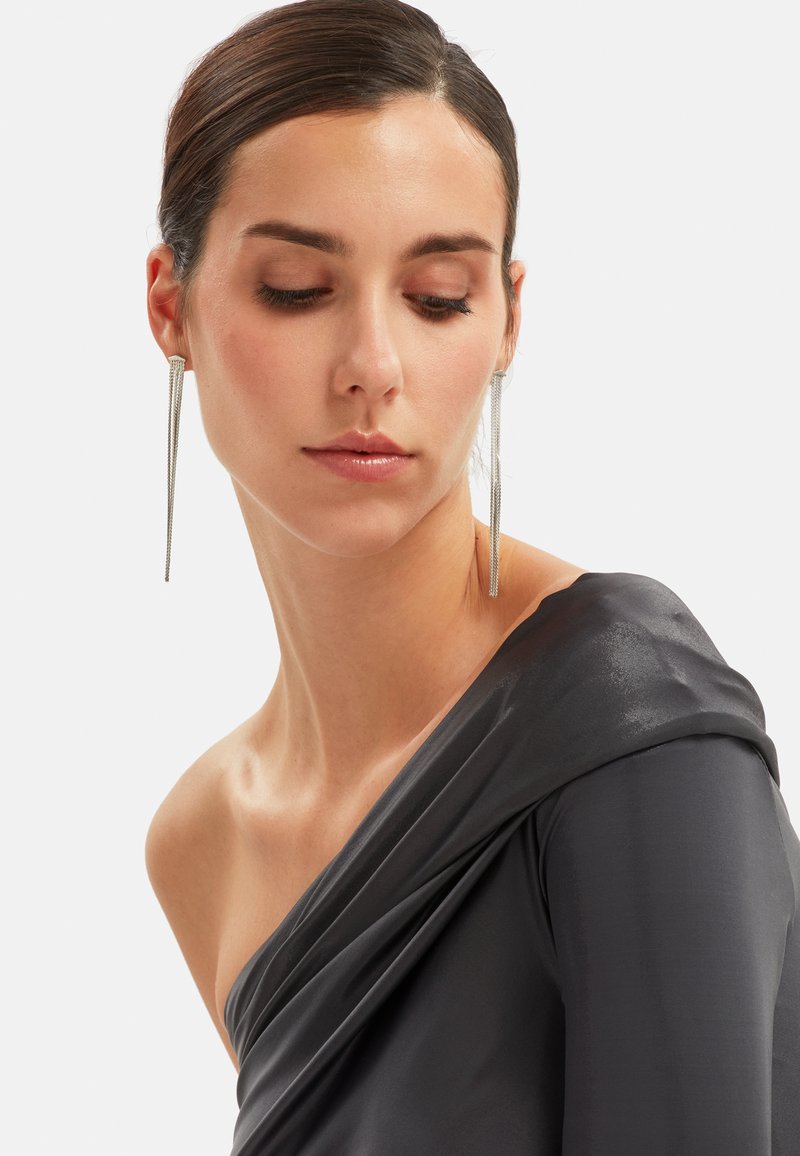 Asymmetrische grijze zijden top met gedrapeerde textuur, met een een-schouder ontwerp. Lange zilveren oorbellen voegen een stijlvolle, moderne accent toe.