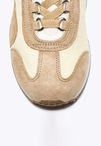 Sneaker beige con upper in camoscio e tela, con accenti marroni, lacci tondi e dettagli cuciti sulla punta e sui pannelli laterali.