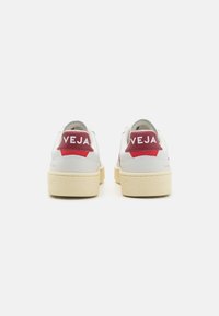 Hvite lær sneakers med en beige gummisåle, røde hæl detaljer og "VEJA" logo. Glatt tekstur med et klassisk lavt design.