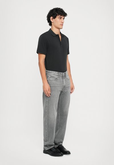 Zwarte poloshirt, grijze denim jeans en zwarte schoenen. Eenvoudig ontwerp, korte mouwen en rechte pasvorm met een lichte vervaging op de jeans.