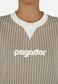 Beige pulóver fehér függőleges csíkokkal, bordázott fehér gallérral, az elején pedig egy feh�ér hímzett "pegador" logóval.