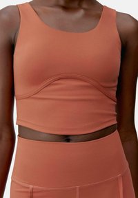 Mjukt fabric crop top i rostfärg. Har en rundad halsringning och böjd sömdetalj över bröstet. Figursydd design.
