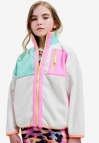Veste en polaire colorée présentant des panneaux turquoise, rose et blanc, avec une fermeture éclair intégrale, un col montant et des accents de fermeture éclair jaunes contrastants.
