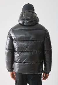 Svart puffjakke med en blank, glatt tekstur, med hette, sydde paneler og elastiske mansjetter. Designet for varme og komfort.