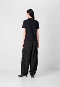Black short-sleeve t-shirt paired with baggy black cargo pants featuring multiple pockets, textured fabric, and pointed black heeled boots.