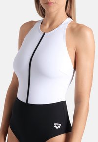 Maillot de bain une pièce en blanc et noir, avec un col haut, fermeture à glissière, et le logo "arena" sur la partie inférieure. Texture de tissu lisse.