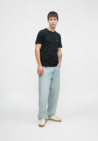Black cotton t-shirt with a small chest logo, paired with light blue baggy denim jeans and cream-colored sneakers.