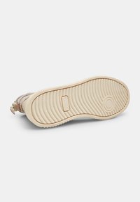 Sole di scarpa con una superficie di gomma testurizzata, colore crema, caratterizzata da una sezione liscia beige e un motivo rotondo incavato.